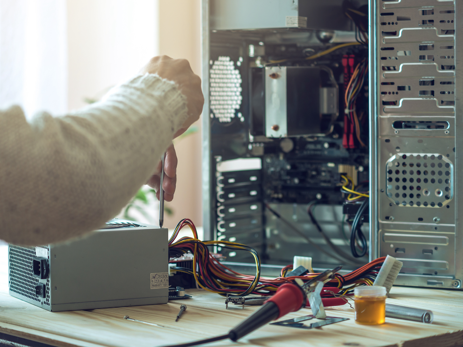 Man repairman is trying to fix using the tools on the computer that is on a workplace in the office. The concept of service electronics and computers.